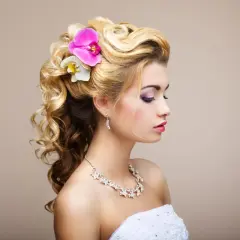 Delikatne fryzury na wesele: blond włosy upięte w loki z kwiatami, ozdobione biżuterią.