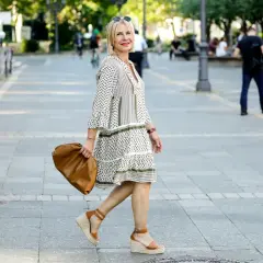 Elegancka kobieta w sukience i espadrylach damskich stylizacjach, z brązową torebką, spaceruje po mieście.