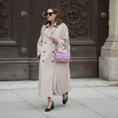 Elegancka kobieta w beżowym płaszczu i liliowej torebce. Pokazuje, jak łączyć kolory, dodając subtelny akcent.
