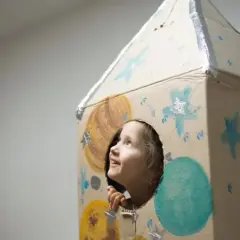Dziecko w kartonowej rakiecie, zapatrzone w gwiazdy, uosabia myślenie życzeniowe i marzenia o kosmicznych podróżach.