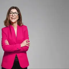 Uśmiechnięta kobieta w różowym żakiecie i okularach, prezentująca styl business formal.