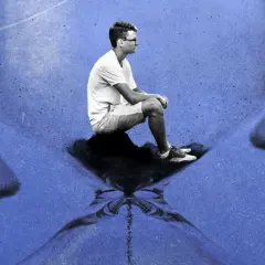 Mężczyzna siedzi na klepsydrze na tle odbicia twarzy.