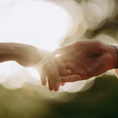 Dłonie splecione w uścisku, symbol miłości i przytulanie od tyłu. Słońce przebija się przez ich palce, tworząc magiczną poświatę.