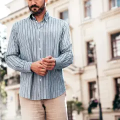 Mężczyzna w pasiowanej koszuli i beżowych spodniach. Dylemat: koszula w spodnie czy nie? Elegancki, miejski styl.