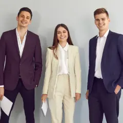 Trzy uśmiechnięte osoby w eleganckich strojach biznesowych. Idealny przykład, jak się ubrać na rozmowę o pracę.
