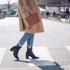 Kobieta w płaszczu i jeansach przechodzi przez pasy, prezentując stylowe botki skarpetkowe. Idealne botki skarpetkowe stylizacje na co dzień.