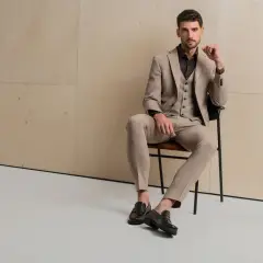 Elegancki mężczyzna w beżowym garniturze, zapatrzony w dal, jakby zastanawiał się, jak ubierają się włoszki.