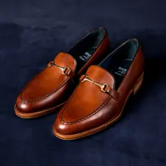 Eleganckie, brązowe loafersy do sukienki z ozdobnym złotym elementem, idealne na specjalne okazje.