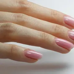 Dłoń z delikatnym, różowym manicurem i pierścionkiem z brylantem. Idealny przykład stylu "clean girl".
