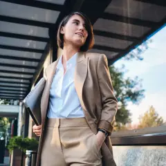 Kobieta w eleganckim stroju, symbolizującym power dressing, trzyma laptopa, gotowa na kolejne wyzwania biznesowe.