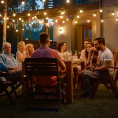 Rodzina i przyjaciele cieszą się wieczorem przy grillu. W tle girlandy światełek i kolorowe chorągiewki tworzą magiczną atmosferę. Idealna garden party stylizacja na grilla.