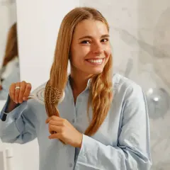 Uśmiechnięta blondynka wykonuje pielęgnację włosów krok po kroku, szczotkując swoje długie, jasne pasma.