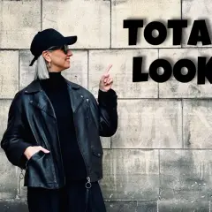 Kobieta w czarnej ramonesce, golfie i czapce prezentuje total look. Stylowe czarne stylizacje to jej znak rozpoznawczy.