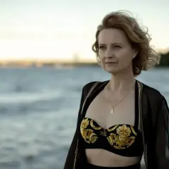 Kobieta w kostiumie kąpielowym i narzutce na plaży, patrząca w dal.
