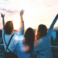 Trzy przyjaciółki wznoszą ręce ku zachodzącemu słońcu. To idealny moment na miłe słowa dla przyjaciółki, pełne radości i wspólnych wspomnień.