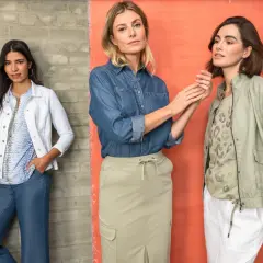 Trzy kobiety w casualowych stylizacjach. Jedna w białej marynarce i dżinsach, druga w dżinsowej koszuli i beżowej spódnicy, trzecia w zielonej kurtce i białych spodniach. Idealny stroj na poprawiny.