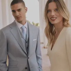 Elegancka para. On w jasnym garniturze, ona w kremowej sukience. Czy na komunie mozna ubrac sie na bialo? Ta stylizacja sugeruje, że tak.