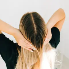 Kobieta z długimi blond włosami, która wciera w skórę głowy wcierkę z kropli żołądkowych.