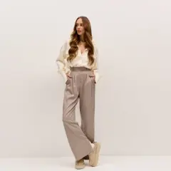 Elegancka kobieta w satynowych spodniach i kremowej koszuli. Idealne buty do teatru? Te wygodne, beżowe botki na platformie dodadzą szyku.