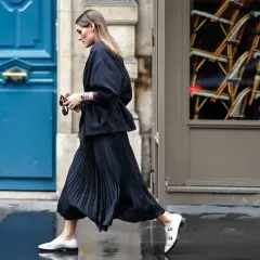 Elegancka kobieta w czarnej spódnicy plisowanej i białych mokasynach przemierza ulicę. Stylowe spódnica plisowana stylizacje.