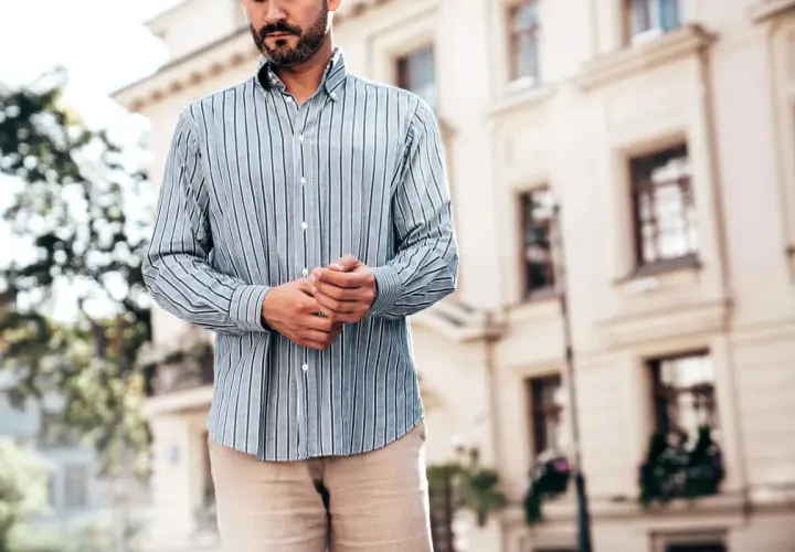 Mężczyzna w pasiowanej koszuli i beżowych spodniach. Dylemat: koszula w spodnie czy nie? Elegancki, miejski styl.