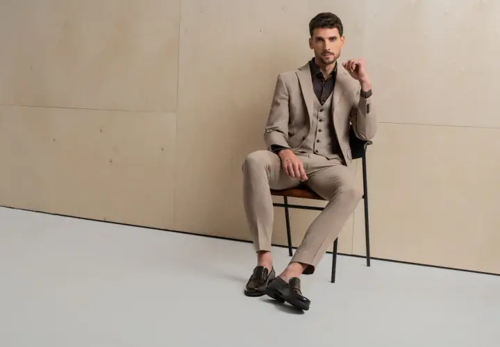 Elegancki mężczyzna w beżowym garniturze, zapatrzony w dal, jakby zastanawiał się, jak ubierają się włoszki.