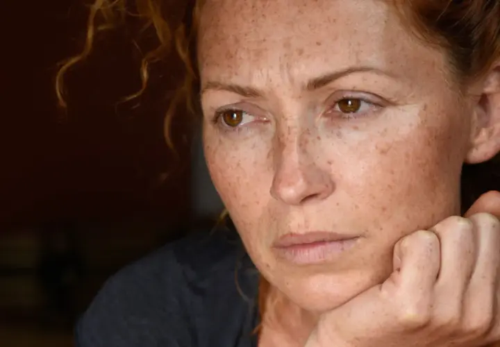Portret kobiety z piegami, zamyślonej, z dłonią podpartą na policzku. Może odzwierciedlać 24 cechy wysoko wrażliwych osób.