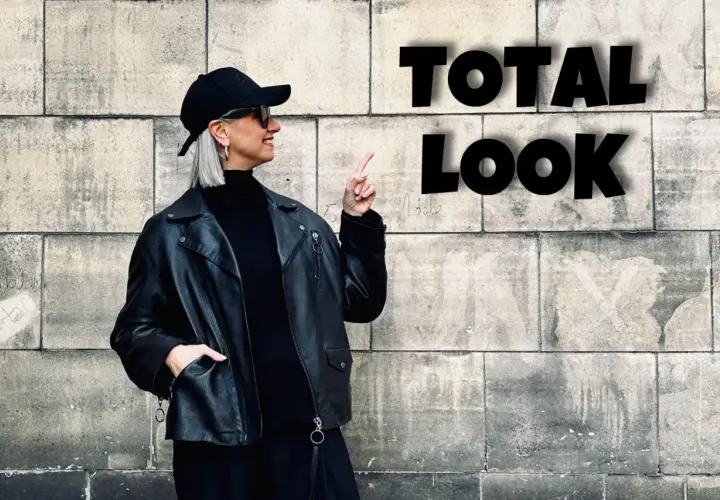 Kobieta w czarnej ramonesce, golfie i czapce prezentuje total look. Stylowe czarne stylizacje to jej znak rozpoznawczy.