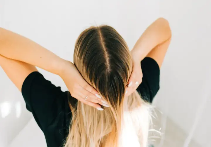 Kobieta z długimi blond włosami, która wciera w skórę głowy wcierkę z kropli żołądkowych.