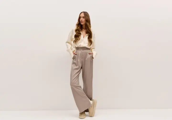Elegancka kobieta w satynowych spodniach i kremowej koszuli. Idealne buty do teatru? Te wygodne, beżowe botki na platformie dodadzą szyku.
