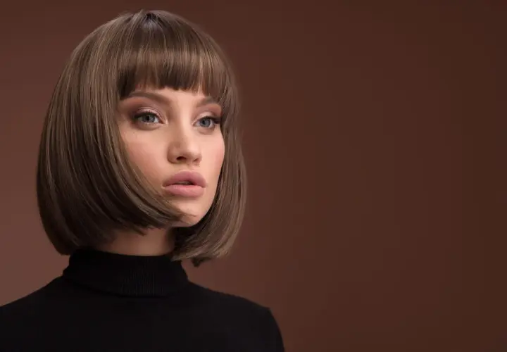 Kobieta z modną fryzurą typu bob i grzywką, w czarnym golfie, na brązowym tle.