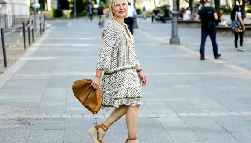 Elegancka kobieta w sukience i espadrylach damskich stylizacjach, z brązową torebką, spaceruje po mieście.