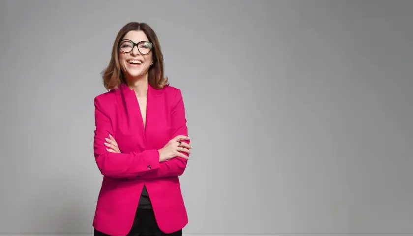 Uśmiechnięta kobieta w różowym żakiecie i okularach, prezentująca styl business formal.