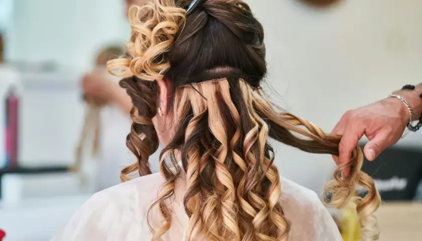 Fryzury na wesele loki włosy średnie. Stylista tworzy loki na średniej długości włosach, dodając objętości i blasku.