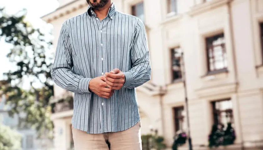 Mężczyzna w pasiowanej koszuli i beżowych spodniach. Dylemat: koszula w spodnie czy nie? Elegancki, miejski styl.