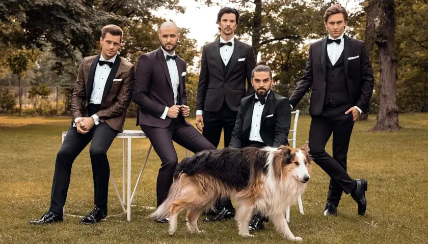 Eleganccy panowie w smokingach i lśniące buty do smokingu, pozują z psem w ogrodzie.