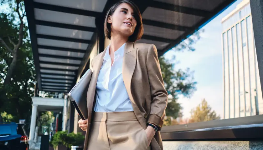 Kobieta w eleganckim stroju, symbolizującym power dressing, trzyma laptopa, gotowa na kolejne wyzwania biznesowe.