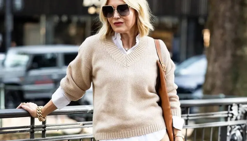 Eleganckie kobiece stylizacje: beżowy sweter, biała koszula, brązowa torebka i złota biżuteria.