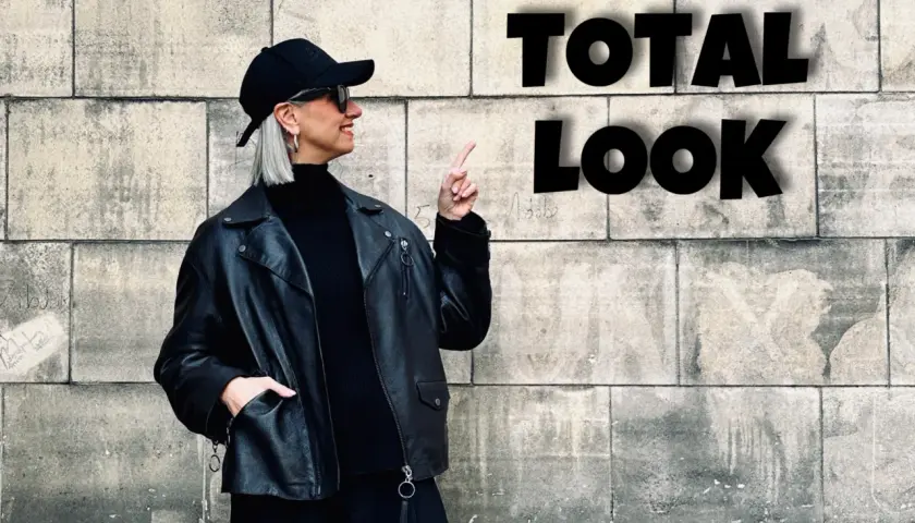Kobieta w czarnej ramonesce, golfie i czapce prezentuje total look. Stylowe czarne stylizacje to jej znak rozpoznawczy.
