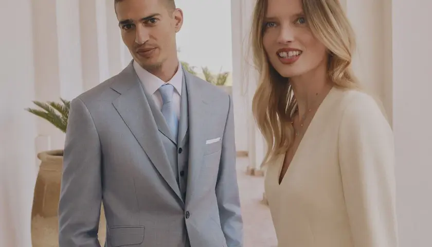 Elegancka para. On w jasnym garniturze, ona w kremowej sukience. Czy na komunie mozna ubrac sie na bialo? Ta stylizacja sugeruje, że tak.