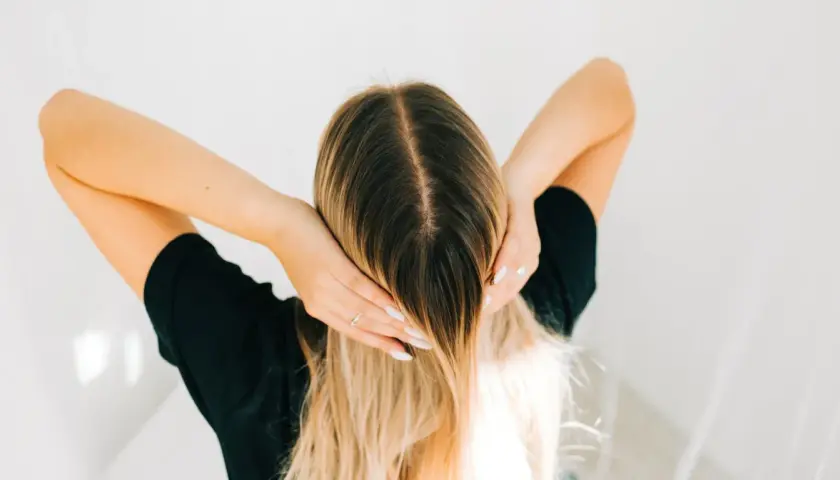 Kobieta z długimi blond włosami, która wciera w skórę głowy wcierkę z kropli żołądkowych.