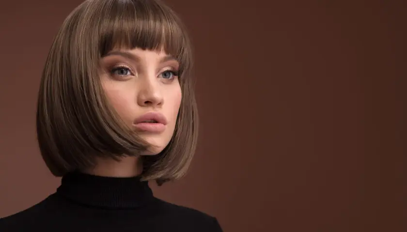 Kobieta z modną fryzurą typu bob i grzywką, w czarnym golfie, na brązowym tle.