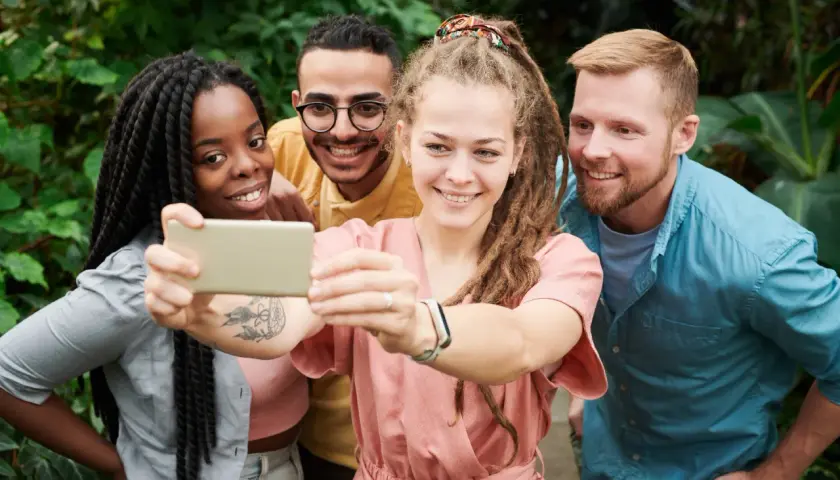 Uśmiechnięci przyjaciele robią selfie w otoczeniu zieleni. Pokazują, że cechy dobrego przyjaciela to wspólne chwile i radość.