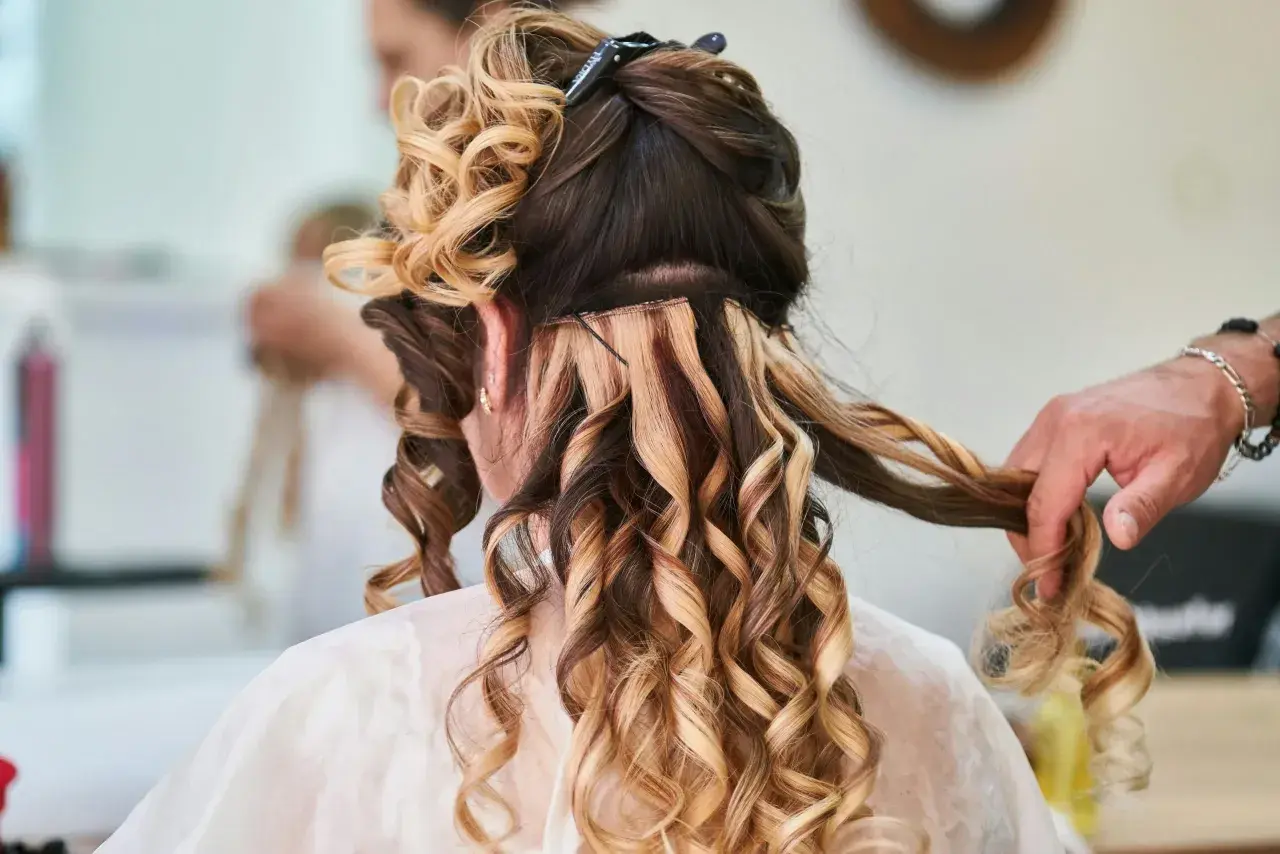 Fryzury na wesele loki włosy średnie. Stylista tworzy loki na średniej długości włosach, dodając objętości i blasku.
