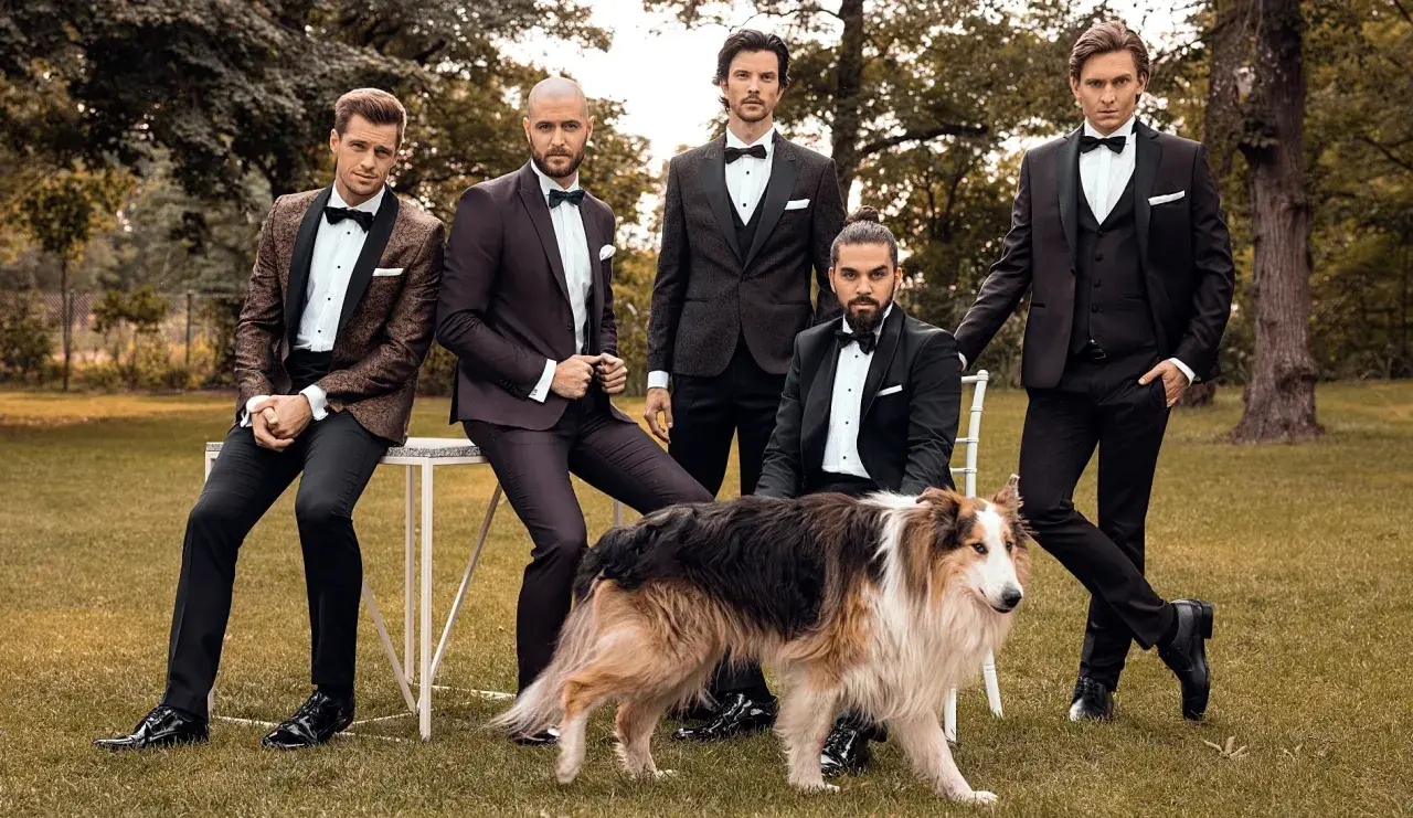 Eleganccy panowie w smokingach i lśniące buty do smokingu, pozują z psem w ogrodzie.