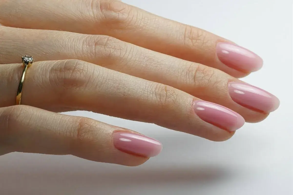 Dłoń z delikatnym, różowym manicurem i pierścionkiem z brylantem. Idealny przykład stylu "clean girl".