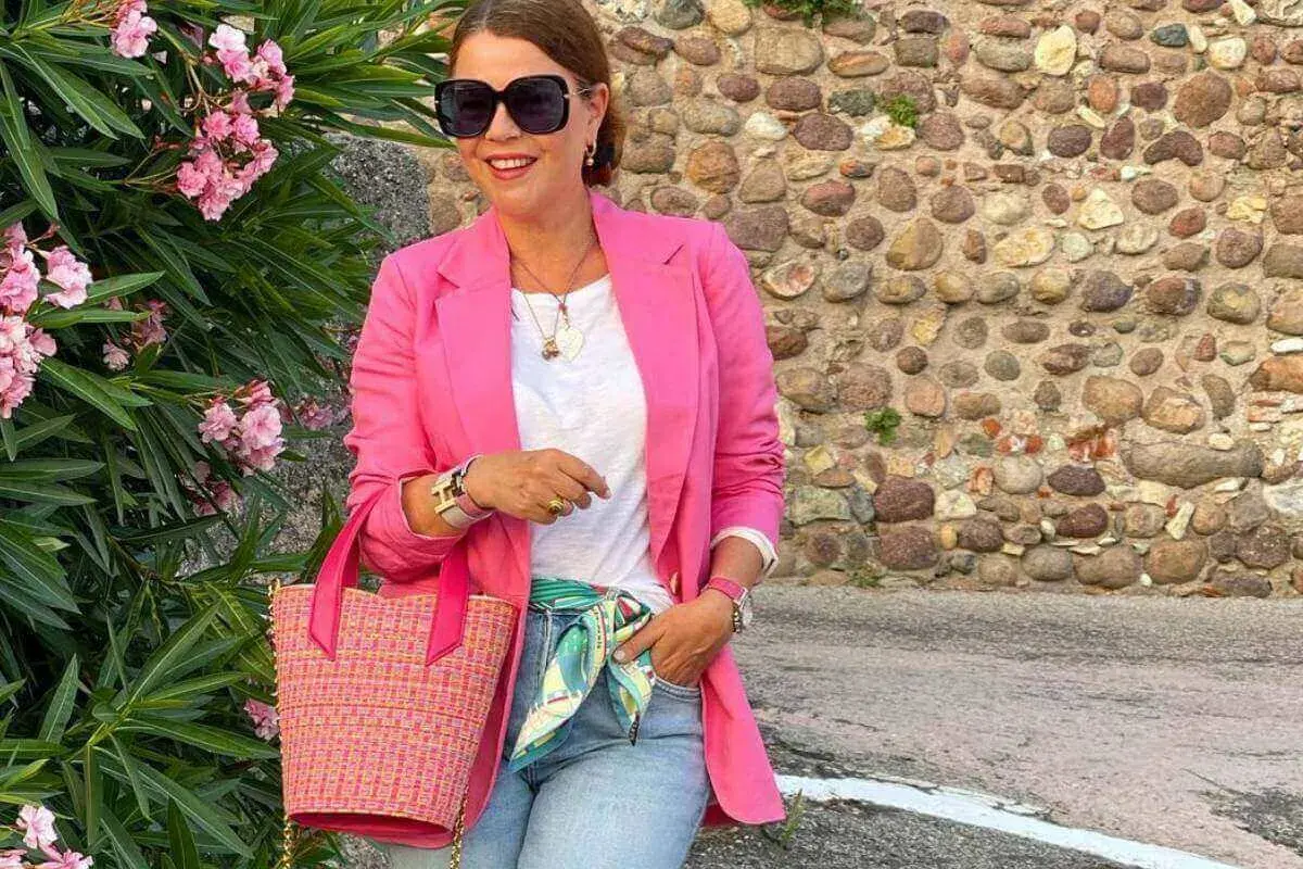 Kobieta w różowej marynarce i jeansach, z torebką i apaszką, tworzy idealny outfit na randkę.