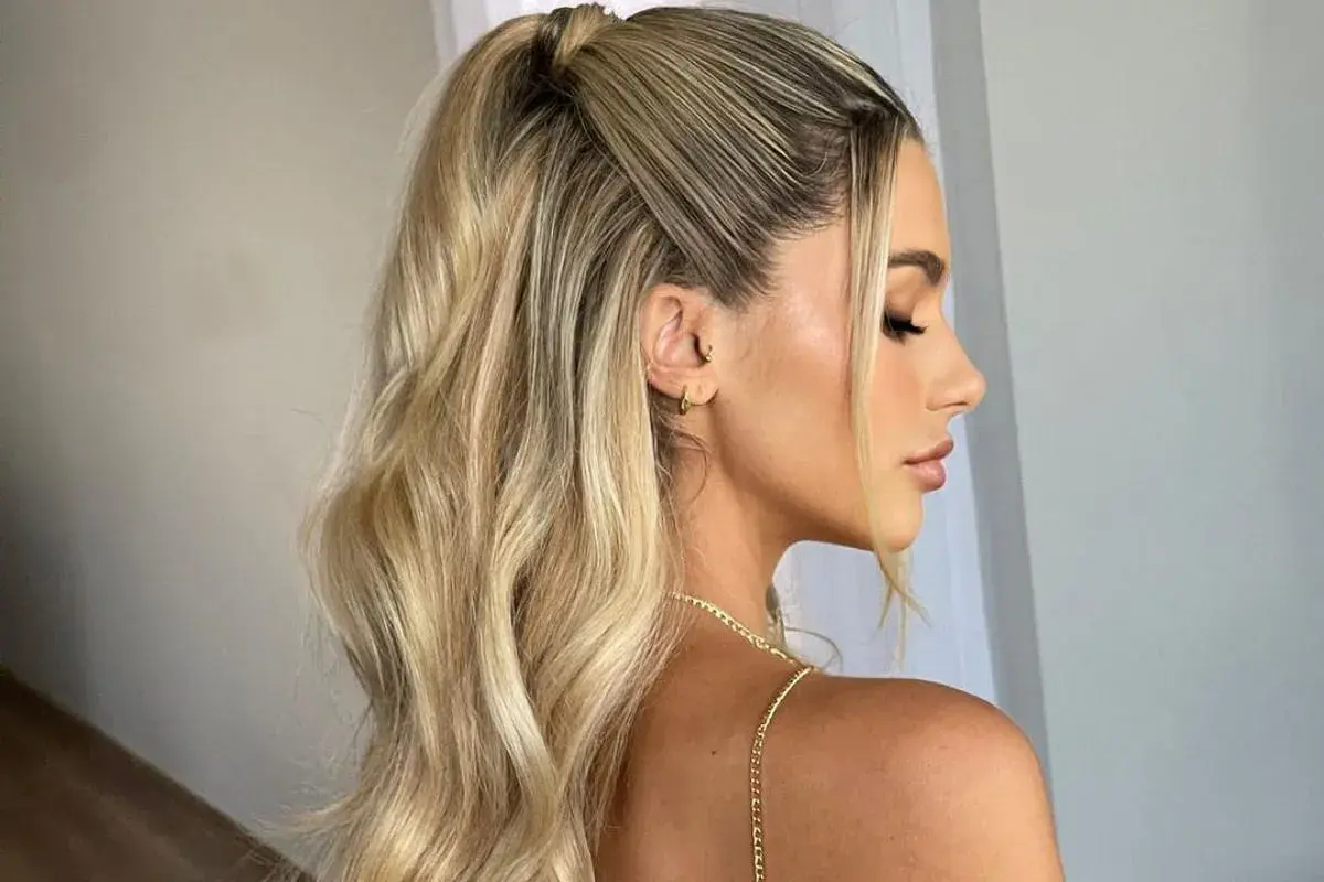 Eleganckie fryzury damskie na wesele: blond włosy upięte w wysoki kucyk z delikatnymi falami i dwoma pasmami opadającymi na twarz.