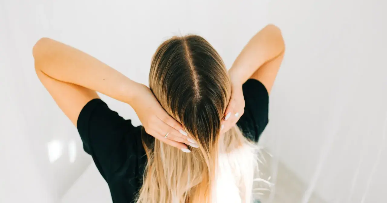 Kobieta z długimi blond włosami, która wciera w skórę głowy wcierkę z kropli żołądkowych.