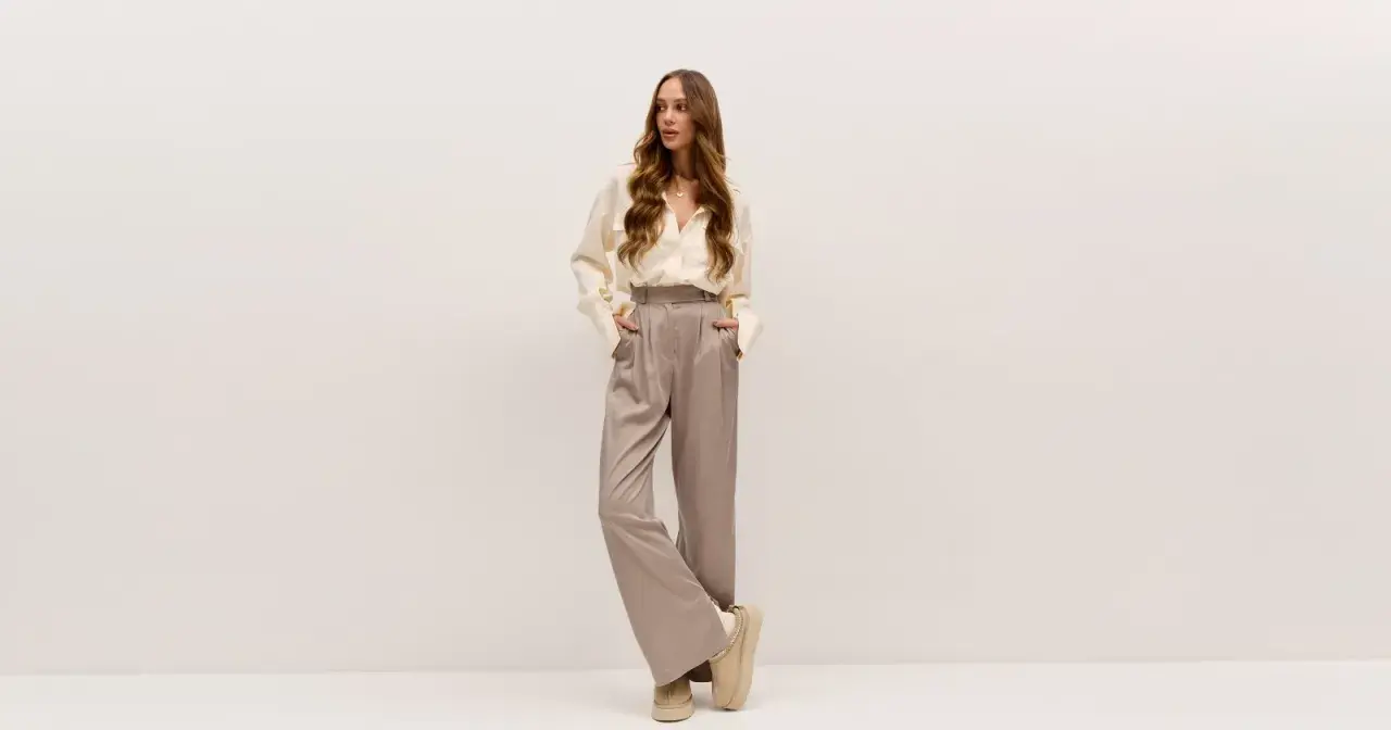 Elegancka kobieta w satynowych spodniach i kremowej koszuli. Idealne buty do teatru? Te wygodne, beżowe botki na platformie dodadzą szyku.